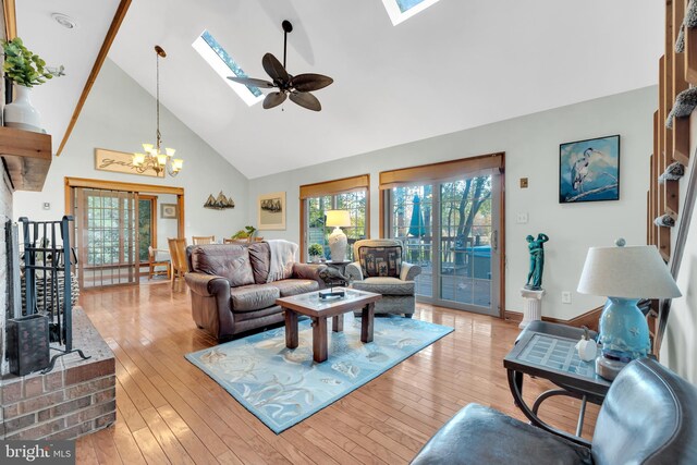 living area featuring ceiling fan with notable chandelier, a skylight, light wood-style flooring, and high vaulted ceiling