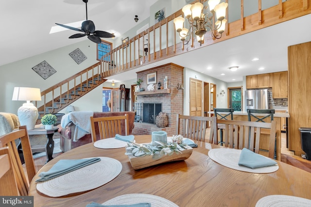 dining space featuring ceiling fan with notable chandelier, recessed lighting, stairway, a brick fireplace, and a towering ceiling