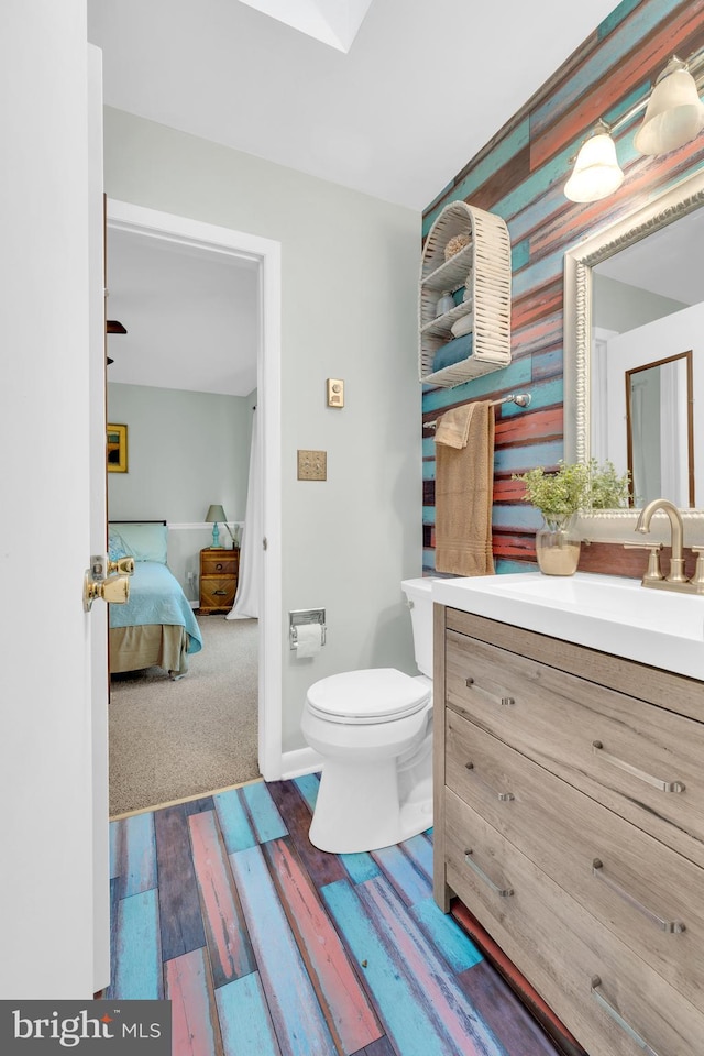 half bathroom featuring toilet, wood finished floors, connected bathroom, baseboards, and vanity