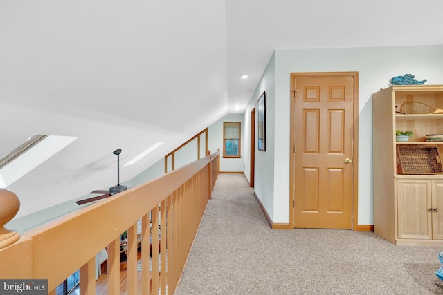 hallway with lofted ceiling with skylight, light colored carpet, and baseboards