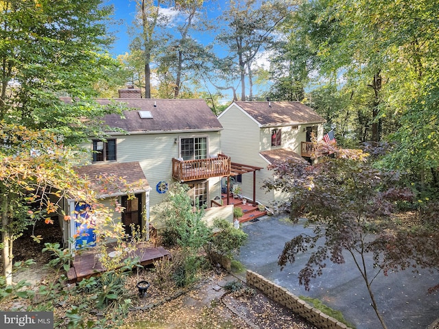 back of house with a wooden deck, a chimney, and roof with shingles