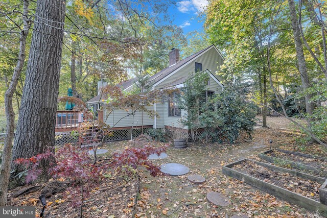 back of property featuring a deck, a garden, roof with shingles, and a chimney