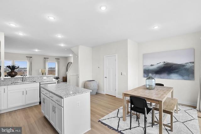 kitchen with light hardwood / wood-style floors, light stone counters, a kitchen island, sink, and white cabinetry