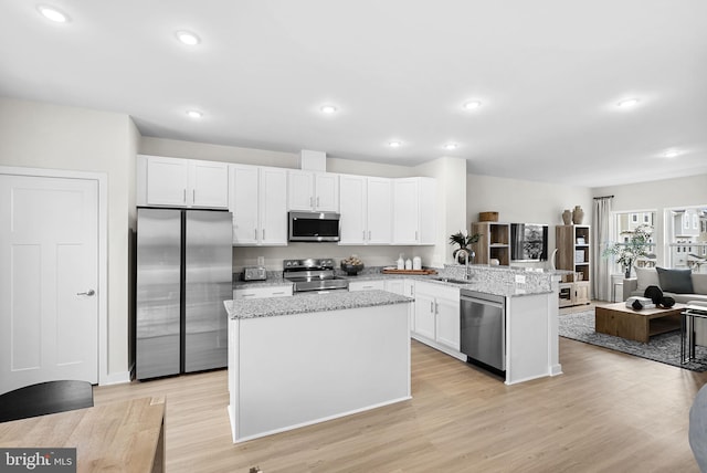 kitchen with stainless steel appliances, kitchen peninsula, sink, light hardwood / wood-style flooring, and white cabinetry