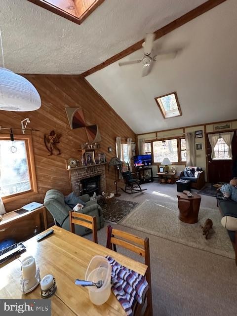 living room featuring a fireplace, a textured ceiling, wooden walls, lofted ceiling with skylight, and ceiling fan