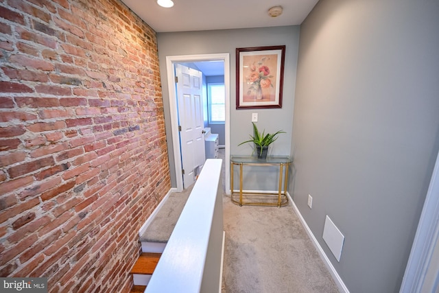 hall with light colored carpet and brick wall