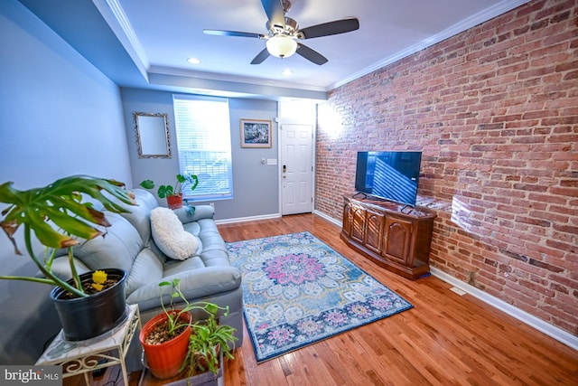 living room featuring light wood-type flooring, ceiling fan, ornamental molding, and brick wall