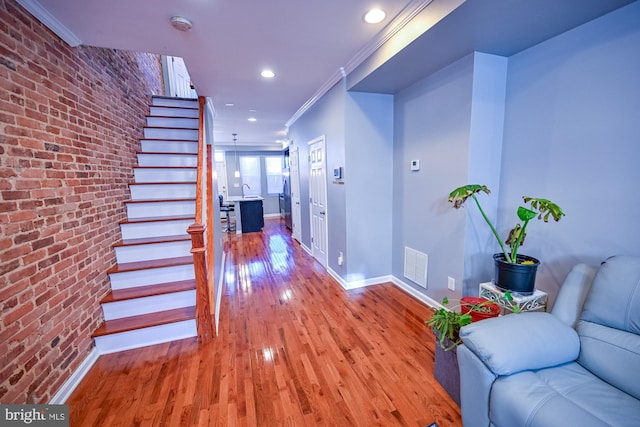 hallway with brick wall, hardwood / wood-style flooring, and crown molding