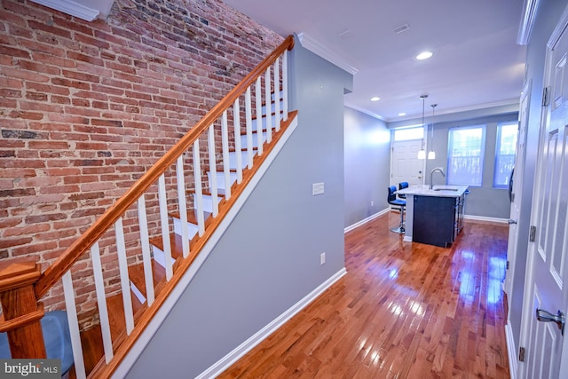 stairway featuring brick wall, sink, hardwood / wood-style flooring, and crown molding