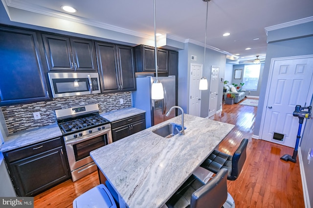 kitchen with stainless steel appliances, light hardwood / wood-style floors, sink, decorative light fixtures, and a kitchen island with sink