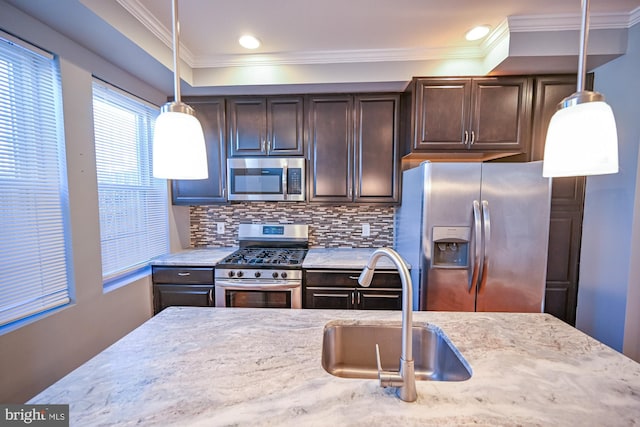 kitchen with dark brown cabinetry, sink, light stone counters, appliances with stainless steel finishes, and decorative light fixtures