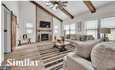 living room with beam ceiling, ceiling fan, a large fireplace, light hardwood / wood-style flooring, and high vaulted ceiling