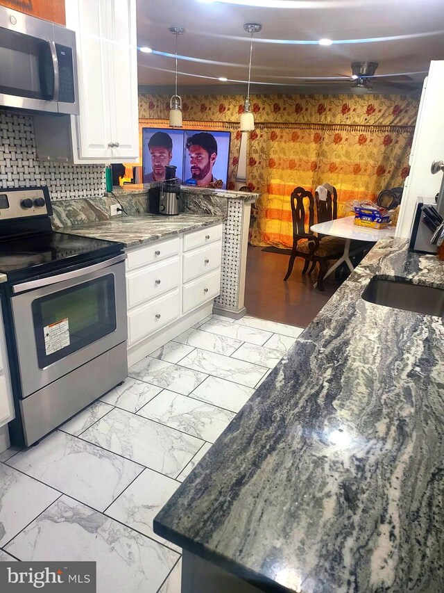 kitchen featuring hanging light fixtures, stainless steel appliances, dark stone countertops, white cabinets, and tasteful backsplash