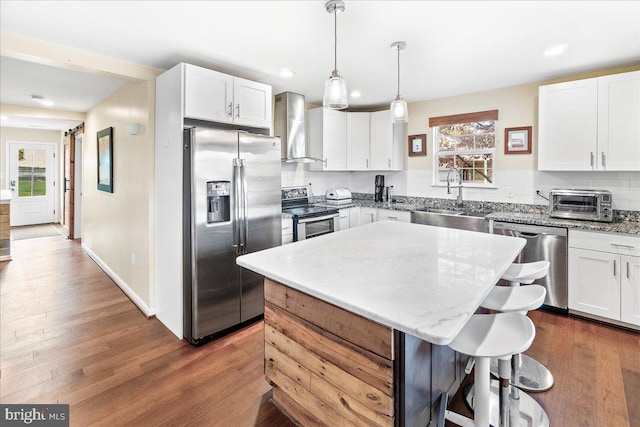 kitchen with wall chimney range hood, sink, a center island, white cabinets, and appliances with stainless steel finishes