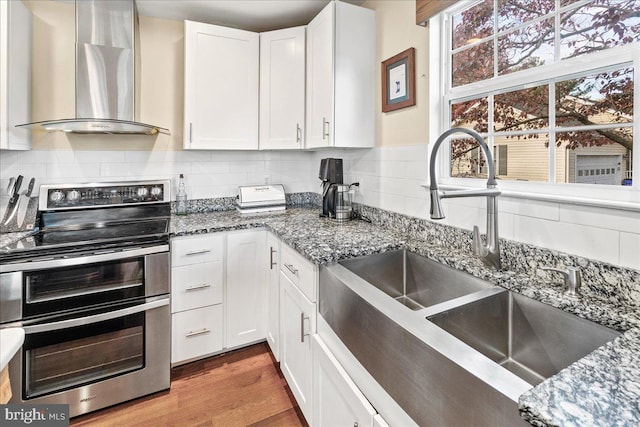 kitchen with stainless steel electric range, white cabinets, hardwood / wood-style floors, wall chimney exhaust hood, and sink