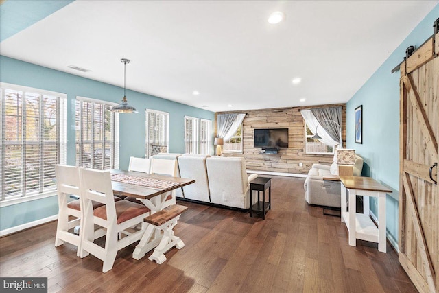 dining space featuring wood walls, dark hardwood / wood-style floors, and a barn door