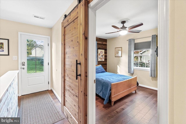 bedroom with ceiling fan, dark hardwood / wood-style floors, multiple windows, and a barn door