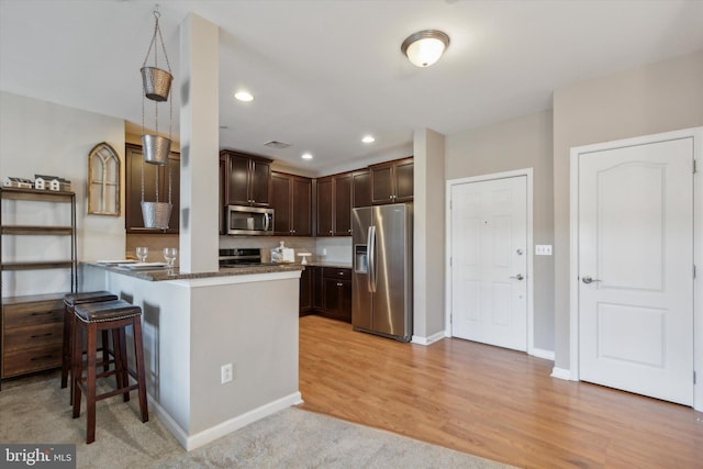 kitchen with dark brown cabinets, a kitchen breakfast bar, light hardwood / wood-style flooring, pendant lighting, and stainless steel appliances