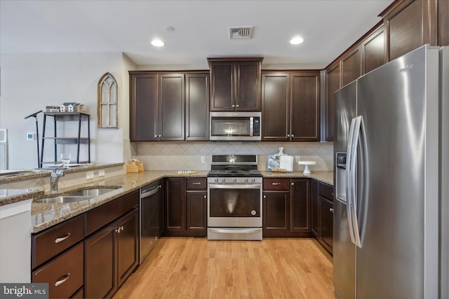 kitchen with light hardwood / wood-style flooring, stainless steel appliances, sink, light stone counters, and tasteful backsplash