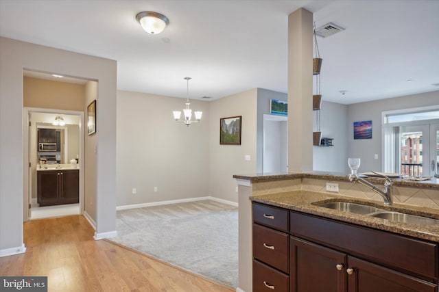 kitchen featuring light hardwood / wood-style flooring, hanging light fixtures, dark stone counters, sink, and an inviting chandelier