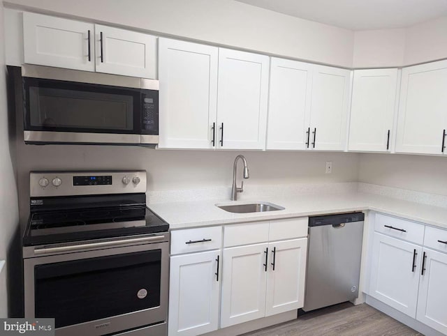 kitchen with sink, appliances with stainless steel finishes, light wood-type flooring, and white cabinetry