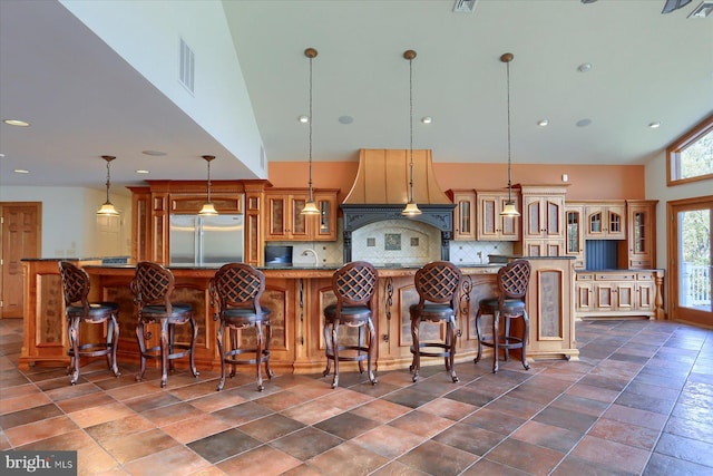 kitchen with a large island with sink, a kitchen breakfast bar, stainless steel fridge, pendant lighting, and high vaulted ceiling