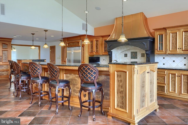 kitchen with hanging light fixtures, backsplash, dark stone counters, high quality fridge, and a center island