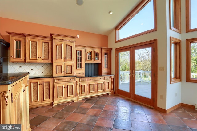 kitchen with dark tile patterned floors, french doors, dark stone countertops, high vaulted ceiling, and tasteful backsplash