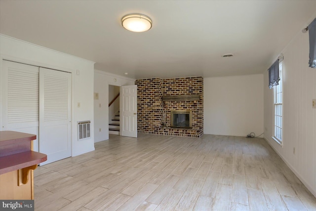 unfurnished living room featuring ornamental molding, a brick fireplace, and light wood-type flooring