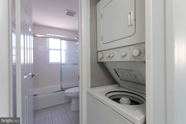 clothes washing area featuring stacked washing maching and dryer and light tile patterned flooring