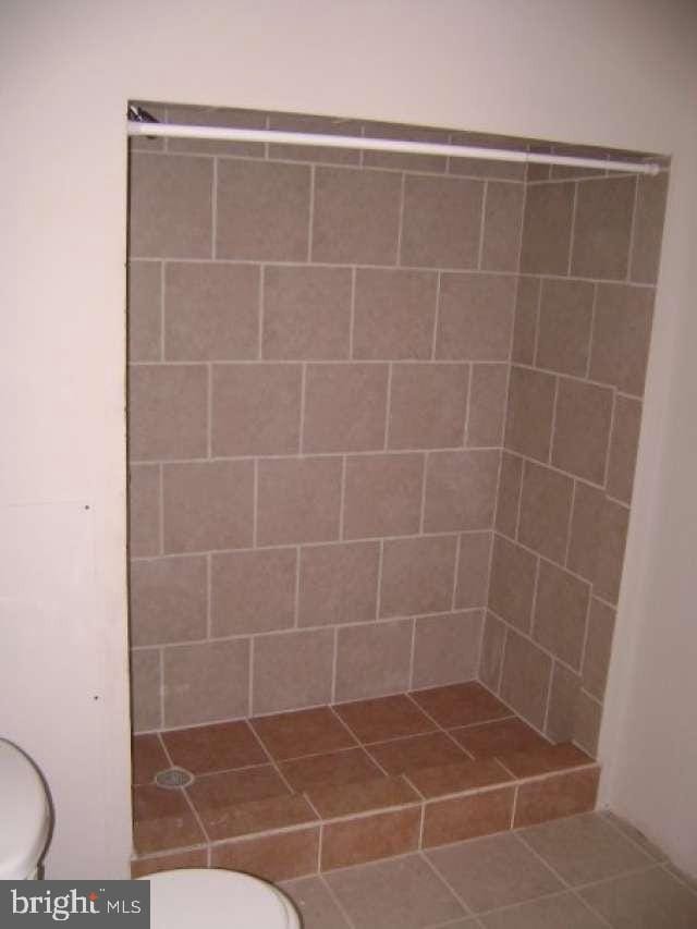 bathroom with tile patterned flooring, toilet, and tiled shower