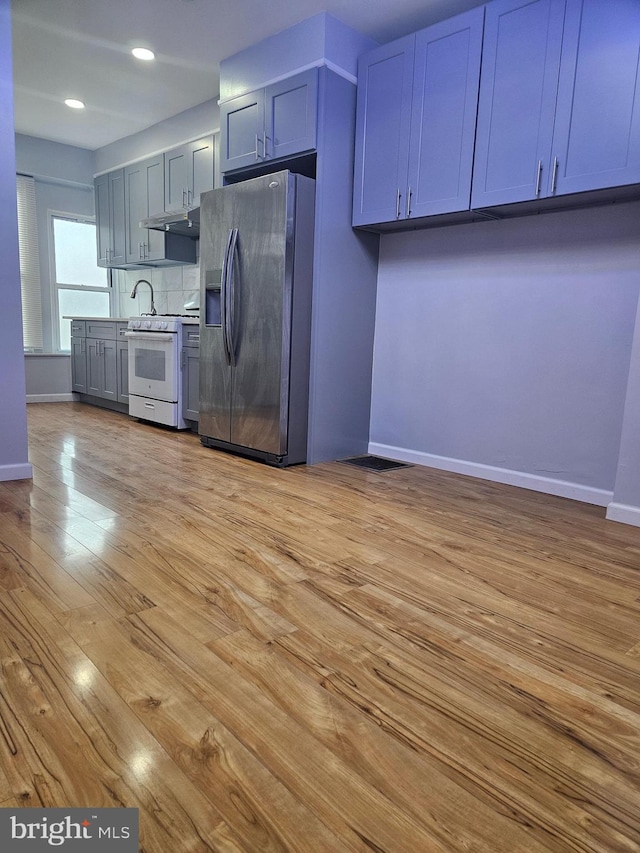 kitchen featuring decorative backsplash, stainless steel fridge with ice dispenser, white gas stove, light hardwood / wood-style flooring, and gray cabinetry