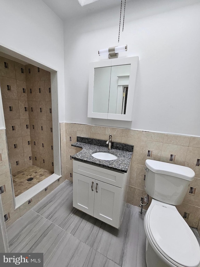 bathroom with tile walls, vanity, a shower, and toilet