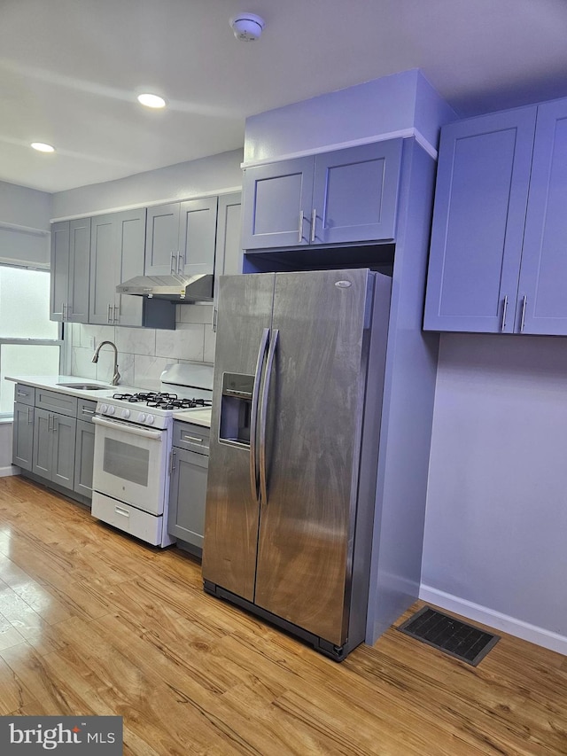 kitchen with white gas stove, sink, stainless steel fridge with ice dispenser, decorative backsplash, and light hardwood / wood-style flooring