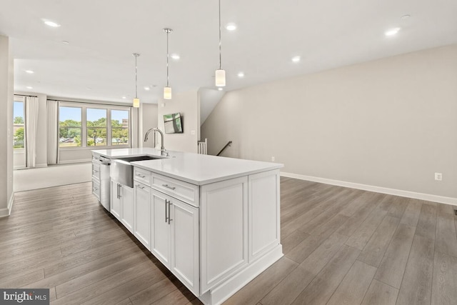 kitchen featuring white cabinets, hanging light fixtures, an island with sink, wood-type flooring, and sink