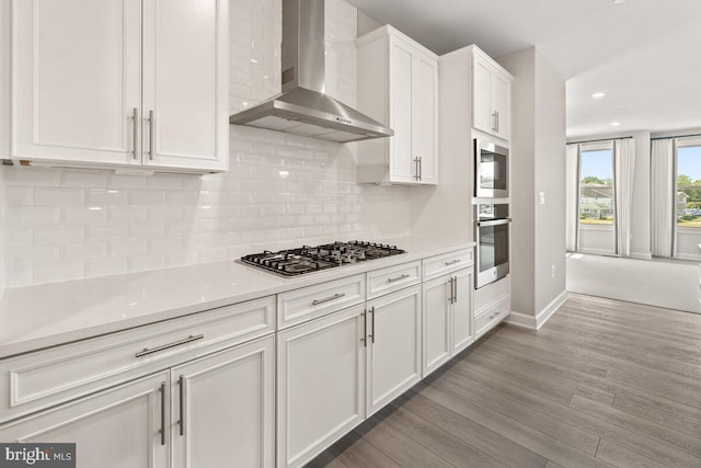 kitchen with decorative backsplash, wall chimney range hood, stainless steel gas cooktop, light hardwood / wood-style flooring, and white cabinetry