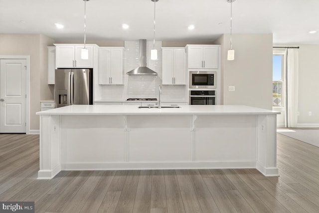 kitchen featuring wall chimney range hood, a large island with sink, appliances with stainless steel finishes, pendant lighting, and sink