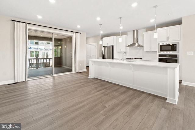 kitchen with a kitchen island with sink, wall chimney exhaust hood, hanging light fixtures, built in microwave, and stainless steel fridge with ice dispenser