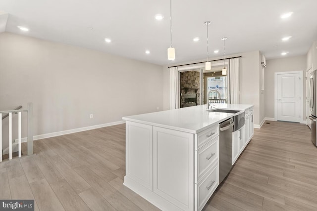 kitchen featuring hanging light fixtures, an island with sink, appliances with stainless steel finishes, white cabinetry, and light hardwood / wood-style floors