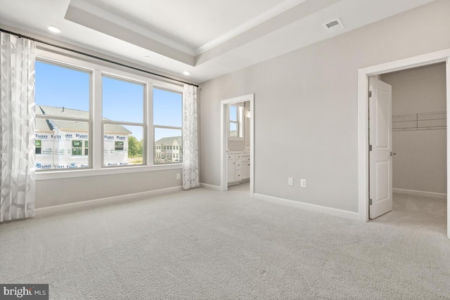 unfurnished bedroom featuring a spacious closet, ensuite bathroom, light colored carpet, and a raised ceiling