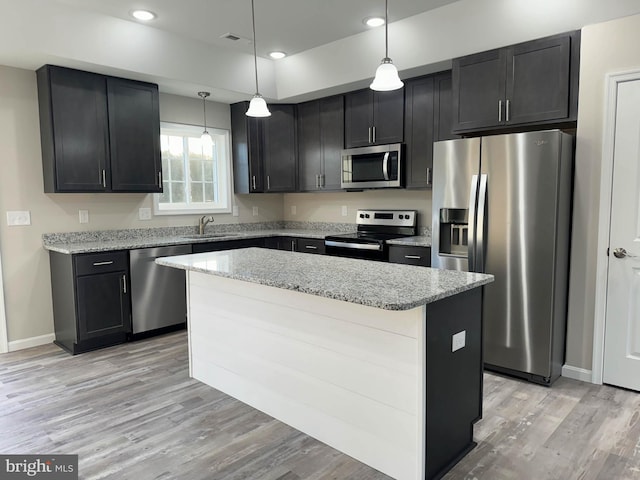 kitchen with light stone counters, appliances with stainless steel finishes, light wood-type flooring, pendant lighting, and a center island