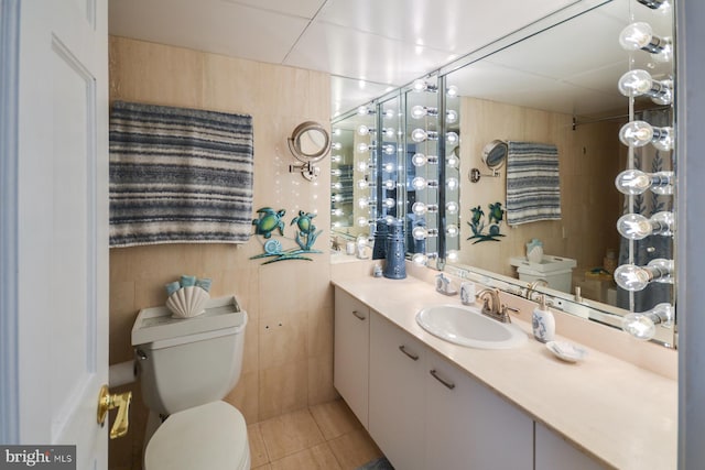 bathroom with tile patterned flooring, vanity, toilet, and tile walls