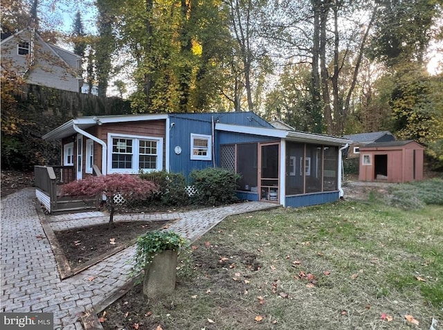 rear view of property featuring a storage shed, a sunroom, and a yard