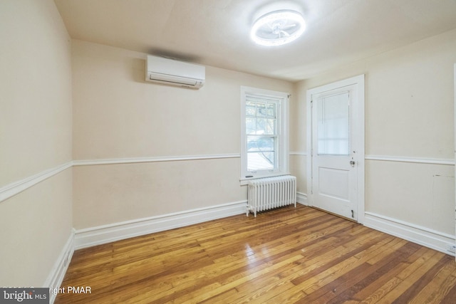 unfurnished room with radiator heating unit, a wall mounted AC, and hardwood / wood-style floors