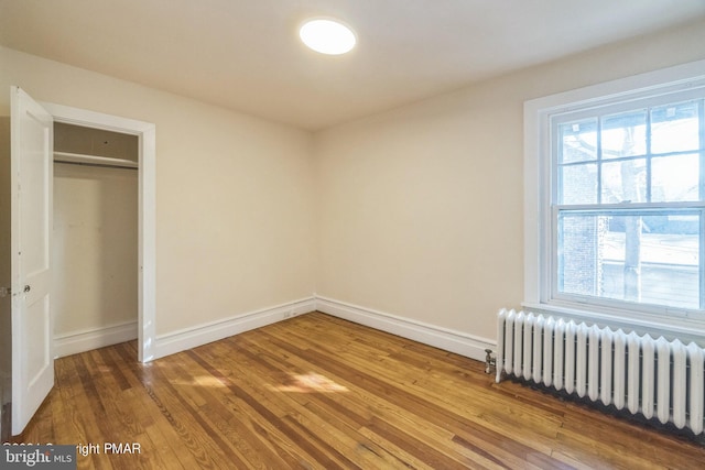 unfurnished bedroom with radiator, a closet, wood finished floors, and baseboards