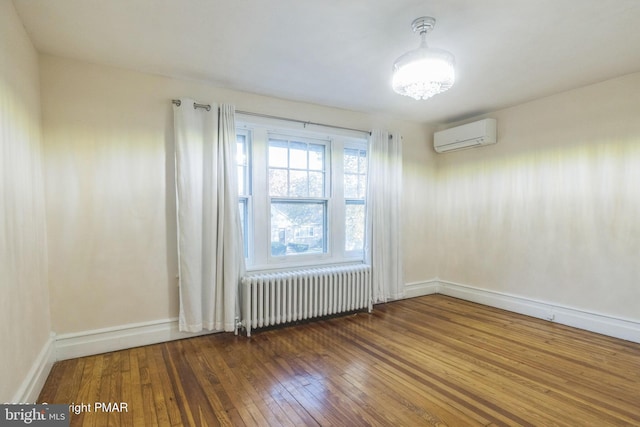 unfurnished room featuring baseboards, a wall mounted air conditioner, radiator, and hardwood / wood-style flooring
