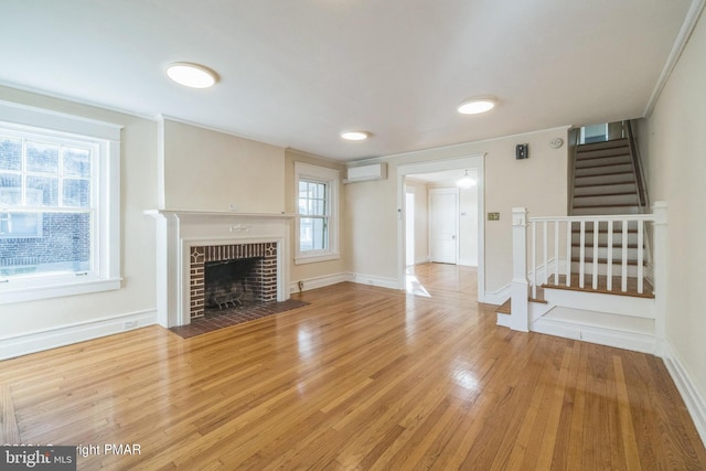 unfurnished living room with a fireplace, stairs, baseboards, an AC wall unit, and wood finished floors