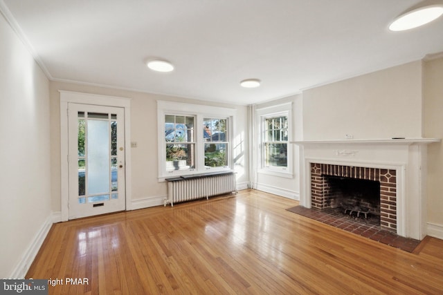 unfurnished living room featuring baseboards, ornamental molding, a brick fireplace, radiator heating unit, and wood finished floors