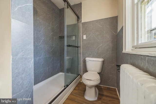 bathroom with radiator heating unit, hardwood / wood-style floors, tile walls, toilet, and a shower with shower door