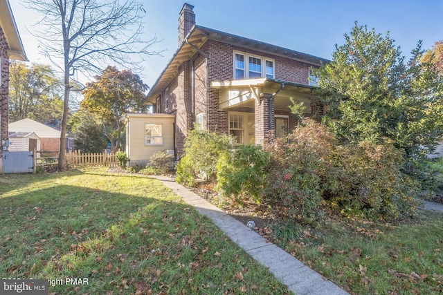 view of side of home featuring a lawn, fence, a chimney, and brick siding